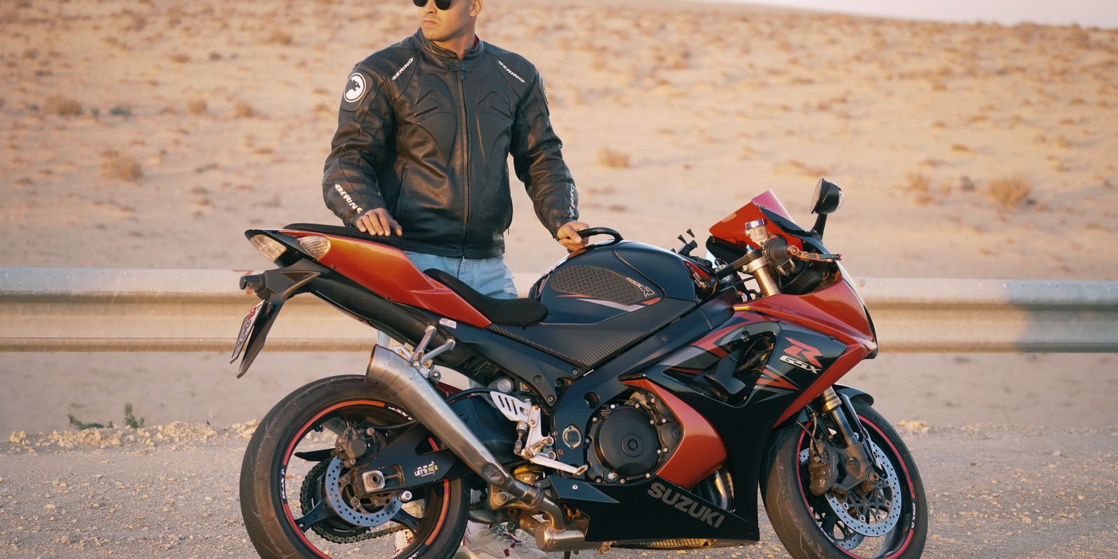 Buneri.es | Bomber, motera o café racer: ¿qué estilo de chaqueta de cuero te queda mejor? Hombre con chaqueta de cuero y gorra posando junto a una moto deportiva en una carretera desértica