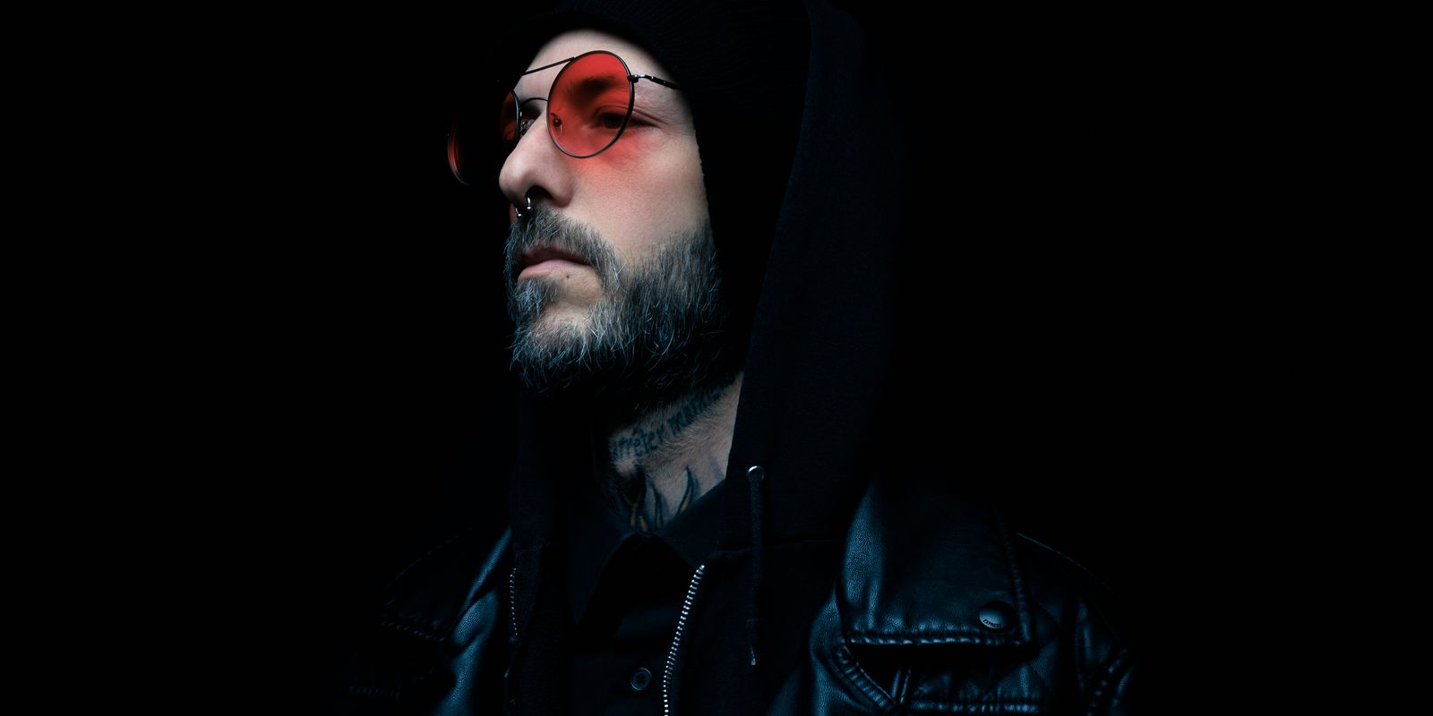 Buneri.es | Chaqueta de Cuero Sobre una Sudadera con Capucha: Cómo Lograr que el Streetwear Funcione Retrato melancólico de un hombre con chaqueta de cuero negra y gafas de tono rojo sobre fondo oscuro