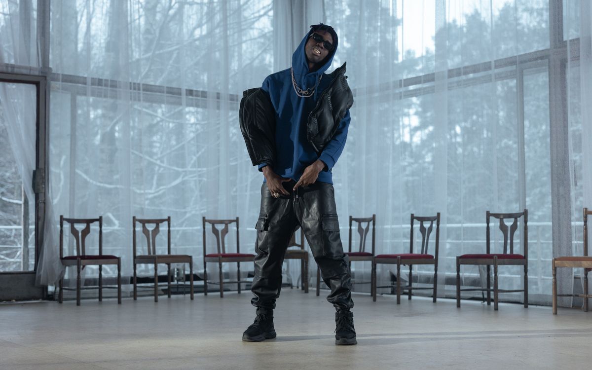 Buneri.es | Chaqueta de Cuero Sobre una Sudadera con Capucha: Cómo Lograr que el Streetwear Funcione Hombre con estilo en sudadera azul y pantalón de cuero posando en interior con iluminación dramática
