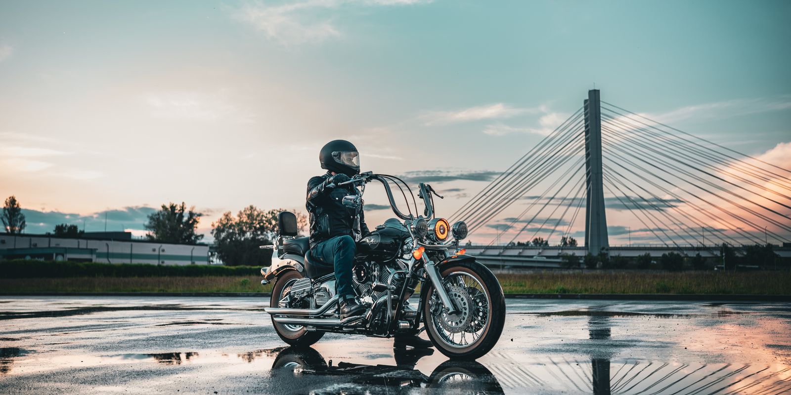 Buneri.es | ¿Se puede llevar una chaqueta de cuero bajo la lluvia? Motociclista con equipo de cuero en una carretera mojada con un puente al fondo al atardecer