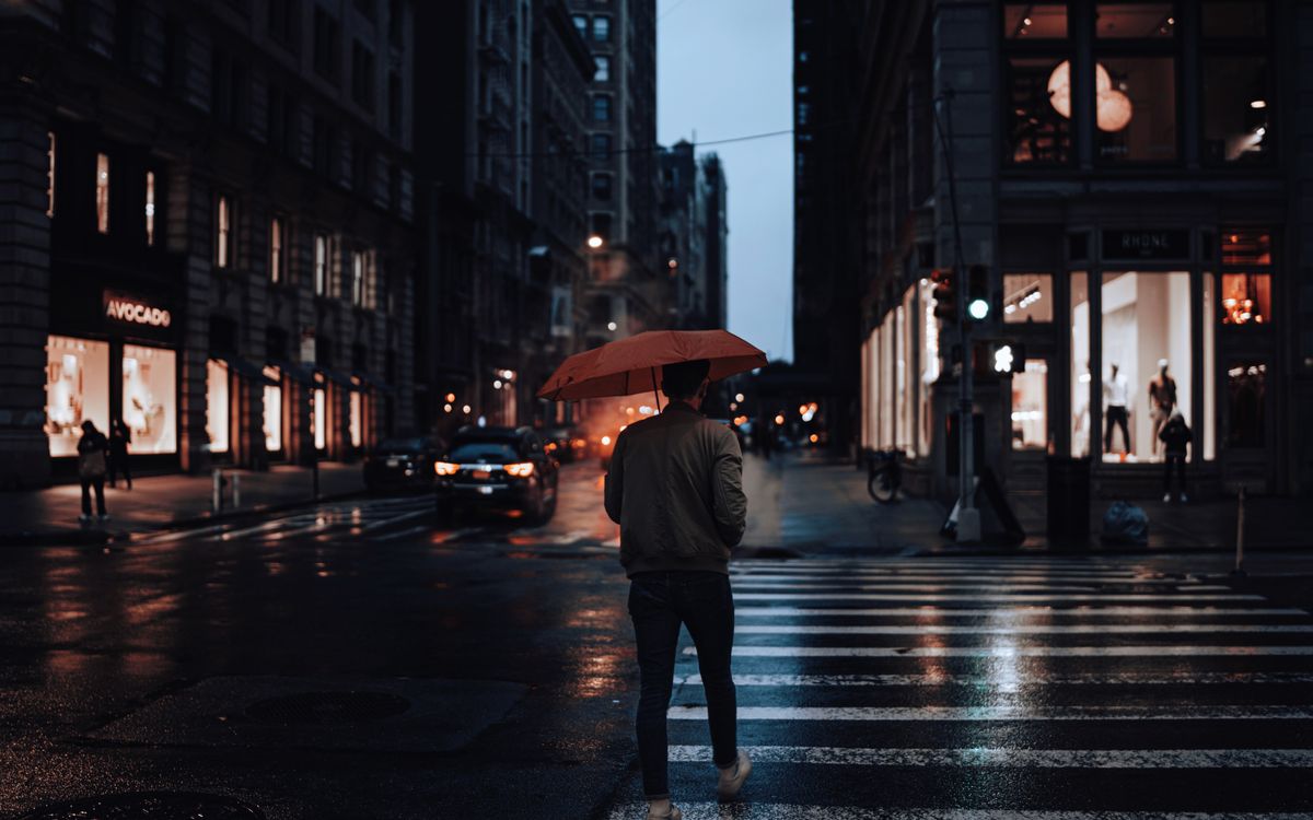 Buneri.es | ¿Se puede llevar una chaqueta de cuero bajo la lluvia? Hombre caminando con paraguas rojo en una calle de ciudad lluviosa de noche