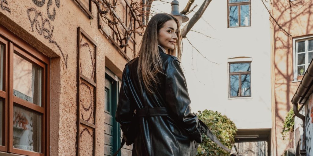 Mujer elegante con un abrigo largo de cuero negro caminando por una calle llena de grafitis