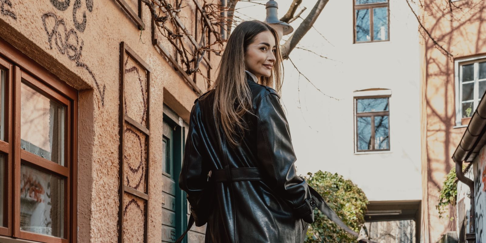 Mujer elegante con un abrigo largo de cuero negro caminando por una calle llena de grafitis