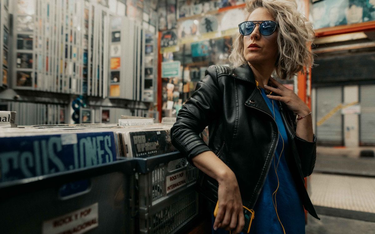 Buneri.es | Cómo Combinar una Chaqueta de Piel con un Vestido Mujer elegante con chaqueta de piel y gafas de sol posando en una tienda de discos de vinilo