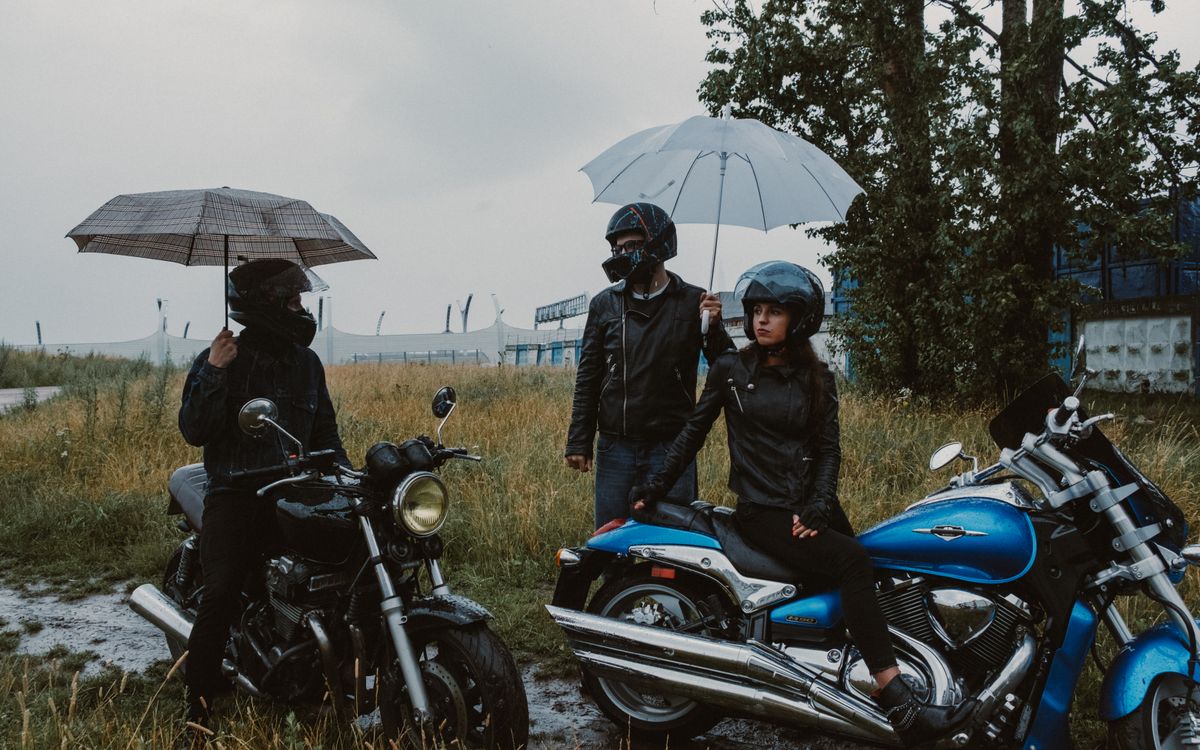 Buneri.es | Cómo Impermeabilizar una Chaqueta de Cuero: Sprays, Ceras y Frecuencia Motociclistas resguardándose de la lluvia bajo paraguas en un campo
