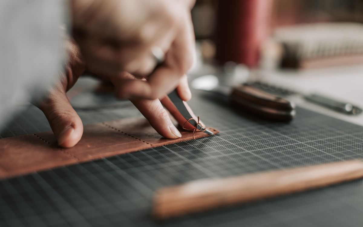 Buneri.es | Cómo Reconocer una Chaqueta de Cuero de Calidad Antes de Comprar Primer plano de manos trabajando minuciosamente una pieza de cuero en un taller