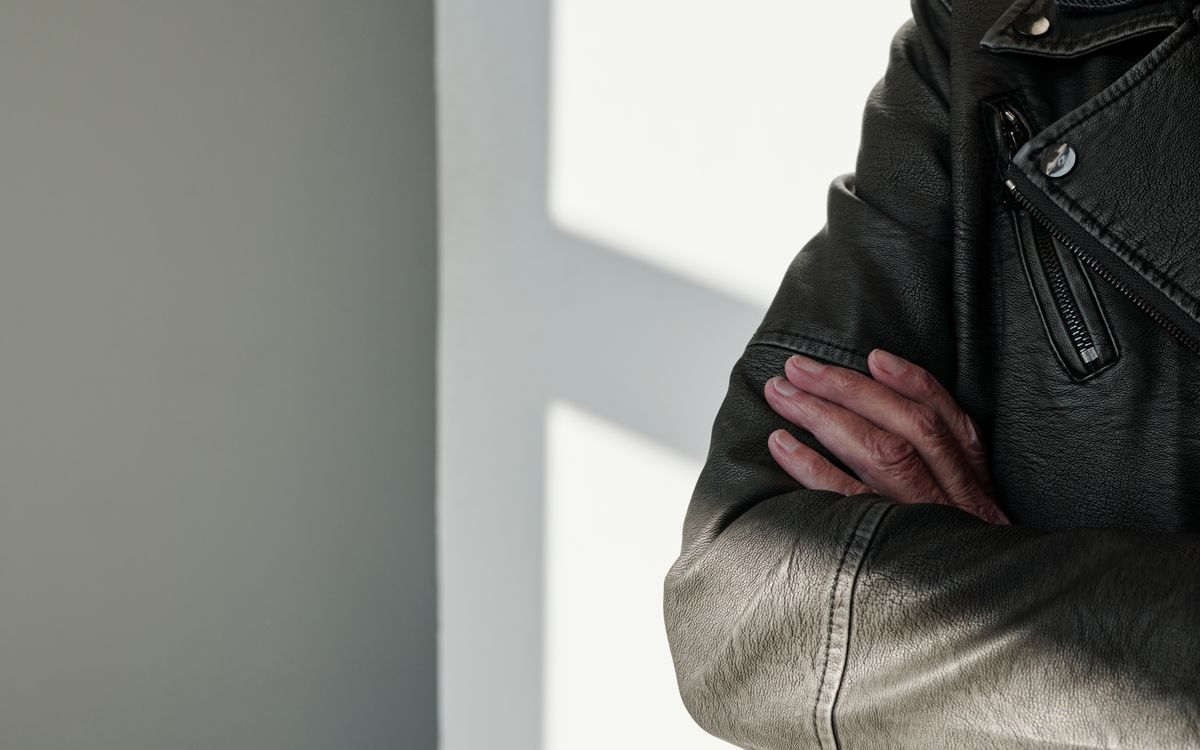 Buneri.es | ¿Cuanto cuesta una chaqueta de cuero autentico (y por que)? Primer plano de brazos cruzados con chaqueta de cuero negro bajo una luz rasante
