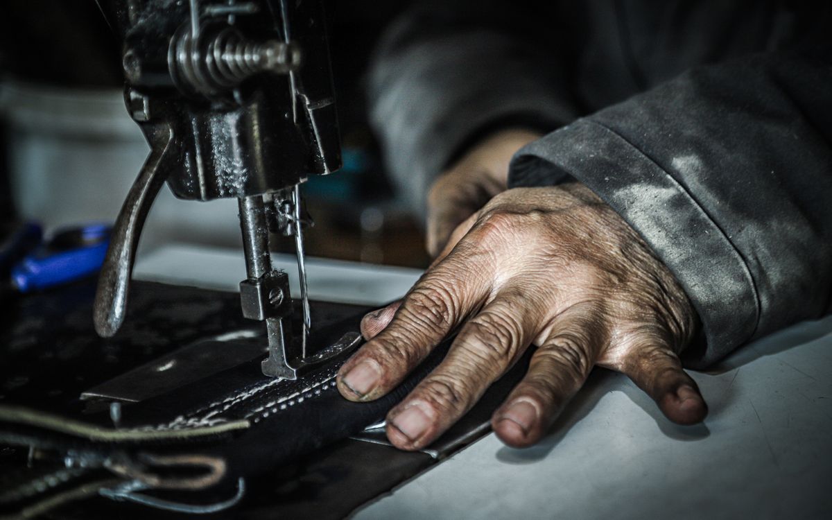 Buneri.es | ¿Cuanto cuesta una chaqueta de cuero autentico (y por que)? Manos guiando el material en una maquina de coser en un taller