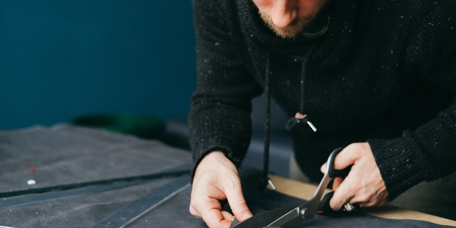 Buneri.es | Reparar una chaqueta de cuero: rotos, arañazos y cremallera Serious male tailor with scissors cutting circle out of leather material while standing at workbench in atelier