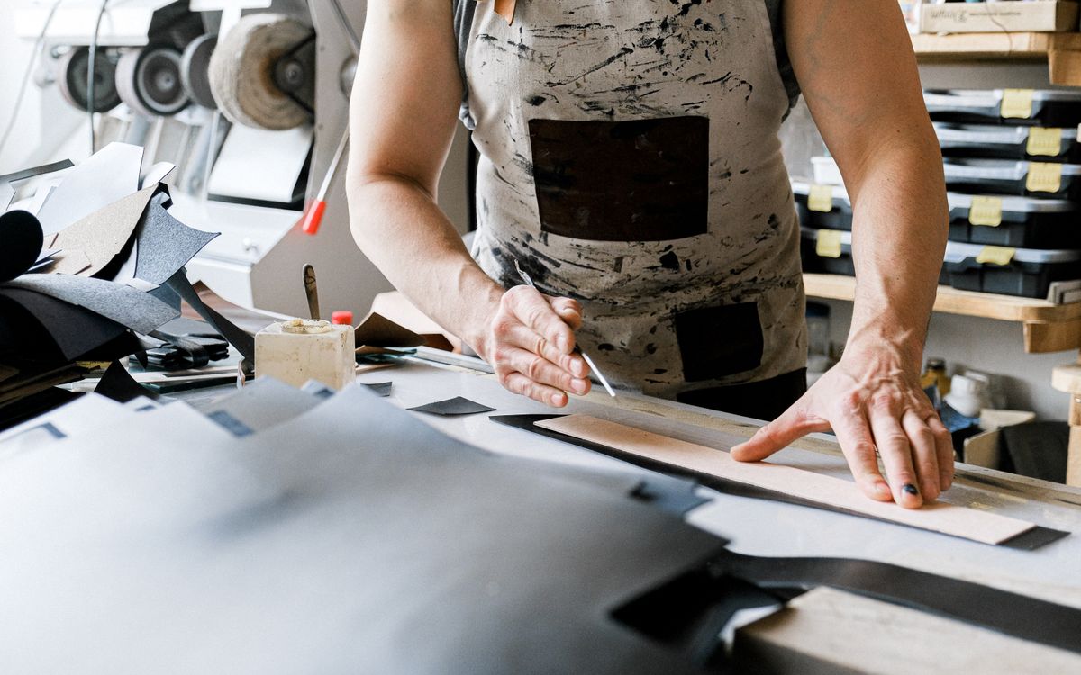 Buneri.es | Reparar una chaqueta de cuero: rotos, arañazos y cremallera A leather artisan actively crafting a piece in a well-equipped workshop, showcasing detailed handiwork