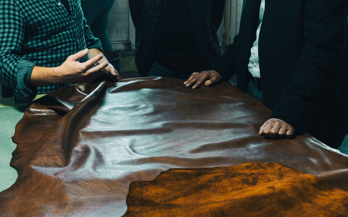 Buneri.es | ¿Vale la pena una chaqueta de cuero auténtico? Grupo de artesanos examinando cuero sobre una mesa, atentos a la calidad y selección del material